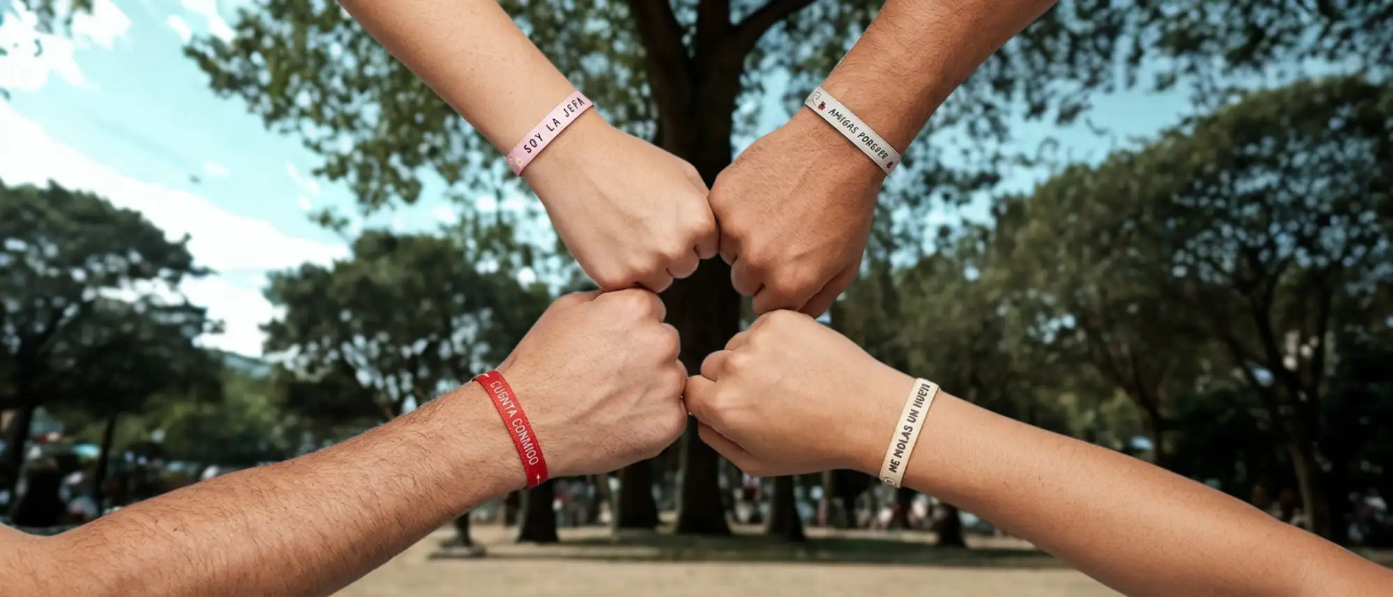 Cuatro manos en un puño, cada una con una pulsera de color diferente con texto impreso.
